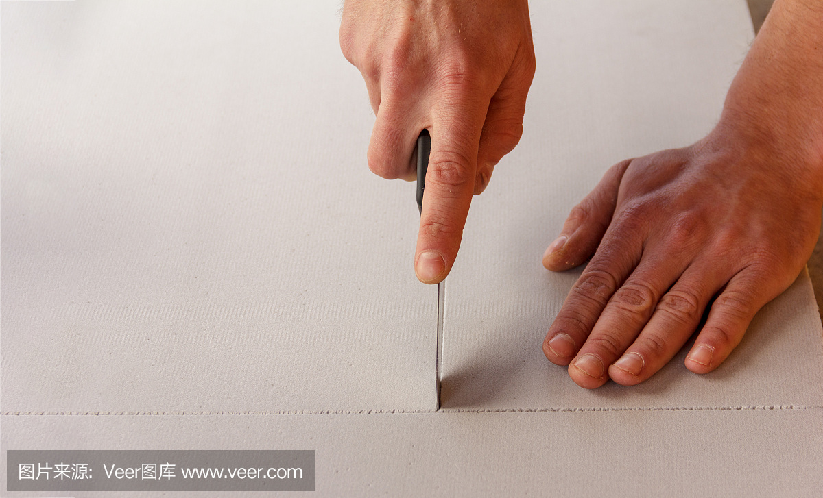 一名男子用文具刀切下一片隔熱隔音材料